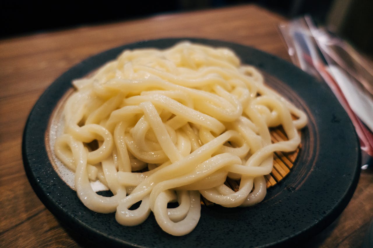 Tantalizing close-up of cooked udon noodles served on an elegant dark plate.